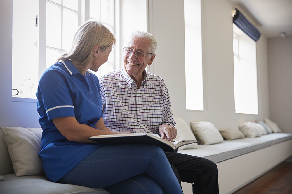 Senior man sitting looking at photo album  with care nurse